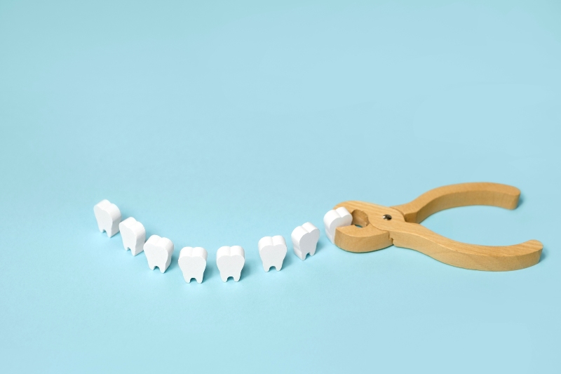 Wooden models of wisdom teeth and pliers on teal background