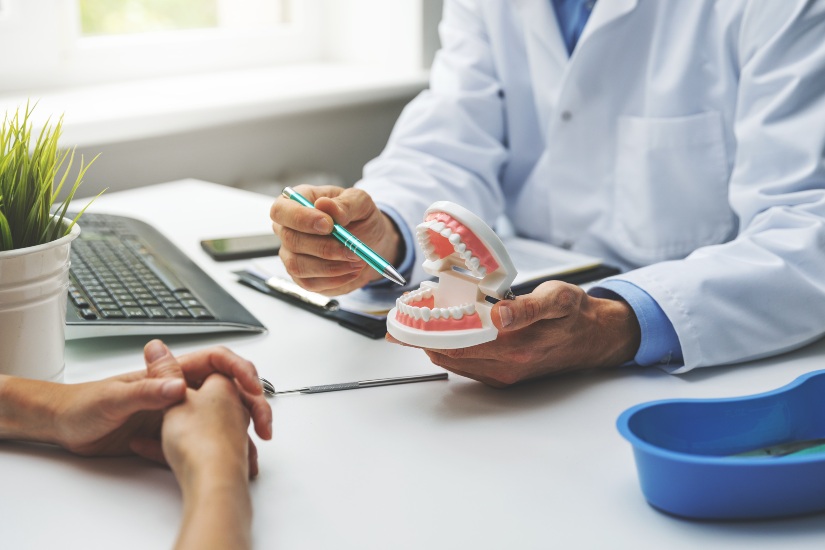 Dentist explaining procedure to a patient holding a plastic model of teeth